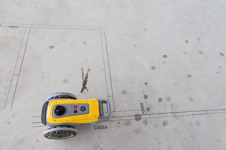 Yellow portable power tool (handheld planer) on a concrete floor with blueprint markings nearby, viewed from above.